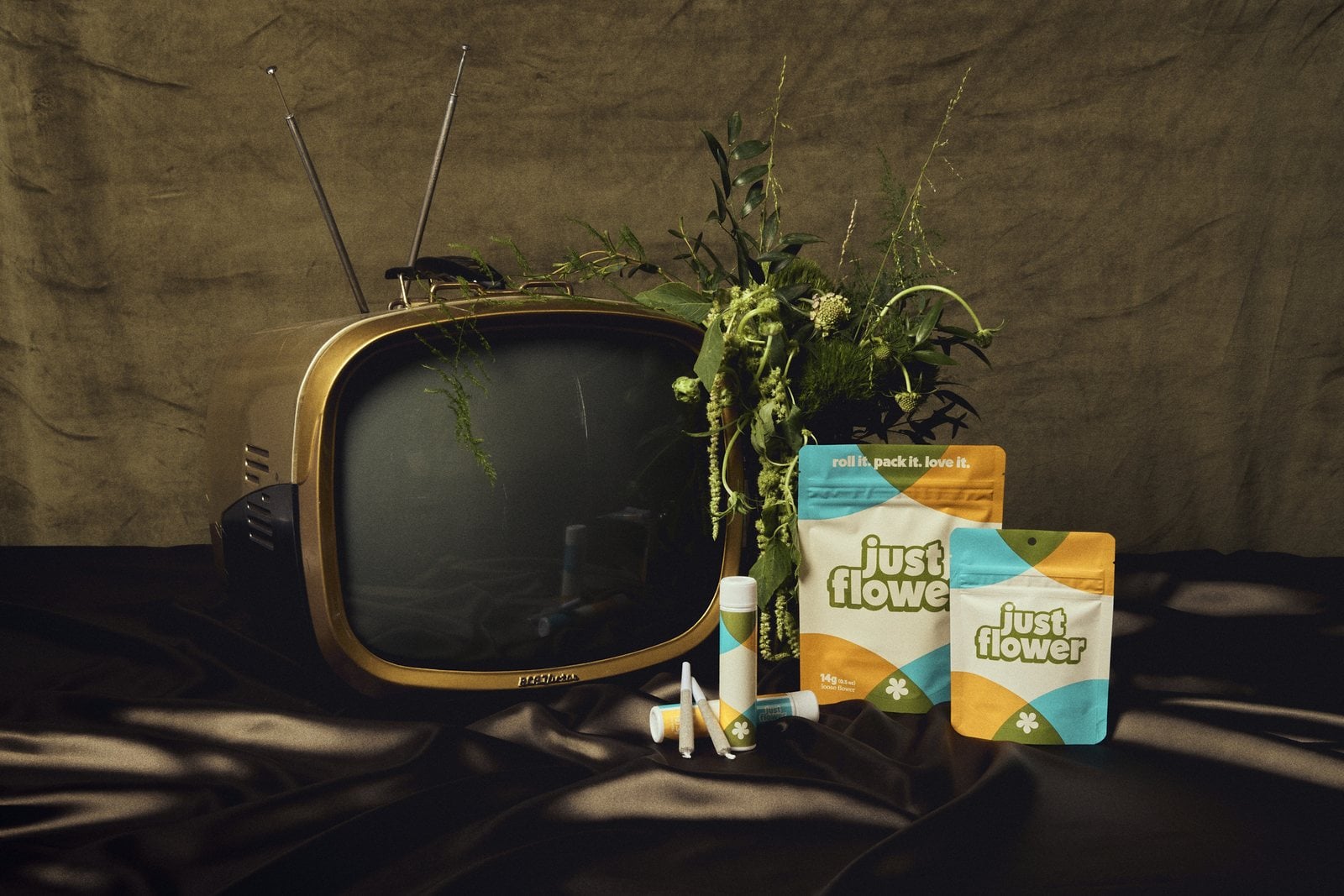 Just Flower cannabis packaging in a retro living-room setting with a vintage television