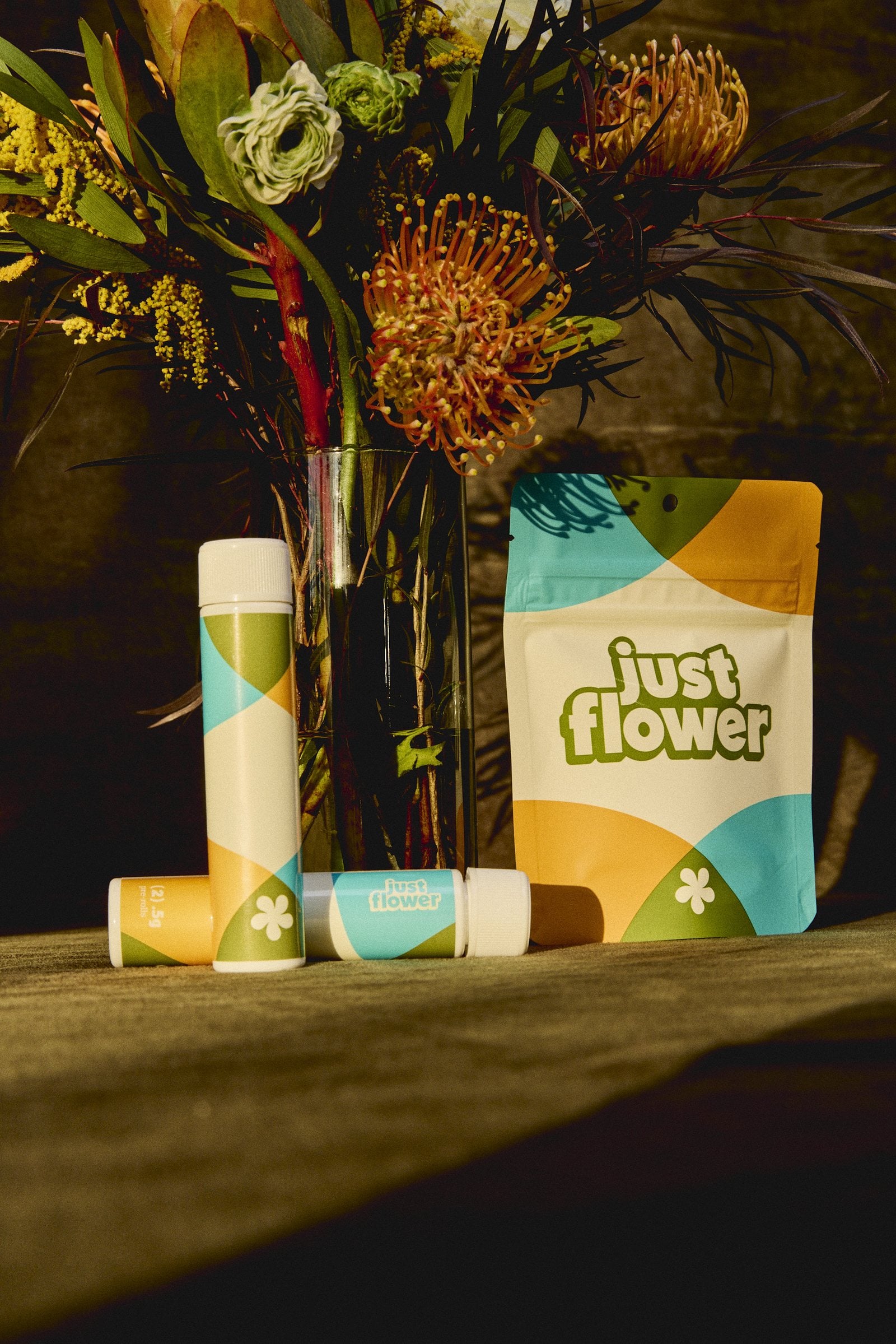 Just Flower cannabis packaging and pre-roll tubes beside a flower arrangement